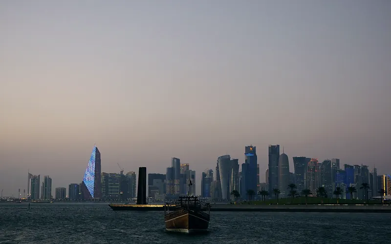 Scenic view of Doha city skyline with traditional dhow boat at dusk along the waterfront