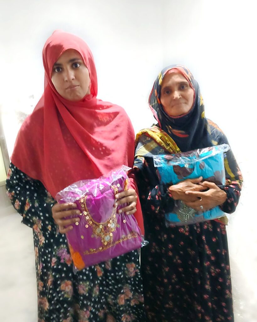 A mother and daughter in Larkana each holding a new suit received through PHWO