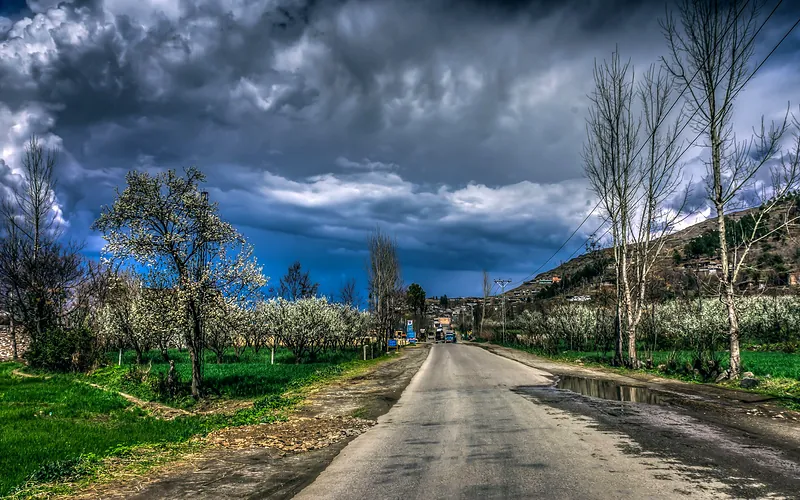 Stunning rural road scene in Kalam, Pakistan with vibrant greenery and dramatic clouds overhead, Khyber Pakhtunkhwa