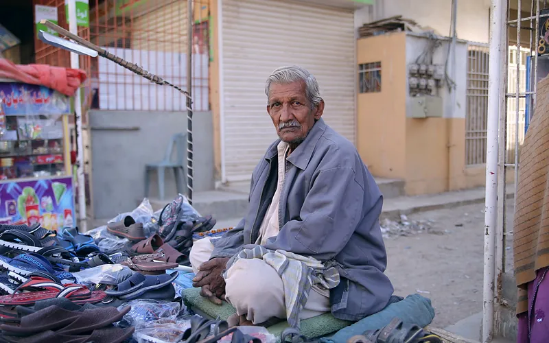 Senior man selling footwear at a street market in Karachi, Pakistan. Local commerce and lifestyle, Sindh