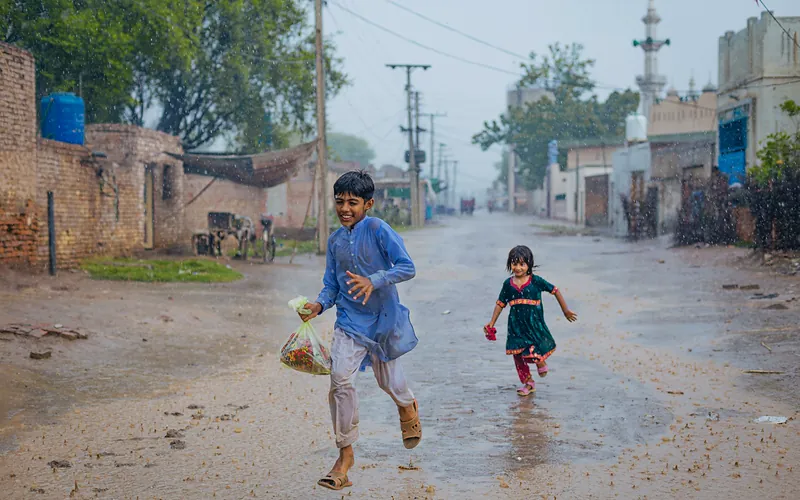 A joyful scene of children running through rain-soaked streets in Sargodha